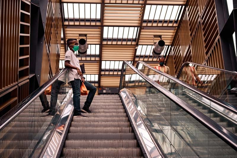 Photo by Darren Clarke showing man standing on escalator wearing green face mask