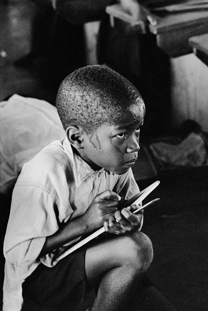 Earnest boy squats on haunches and strains to follow lesson in South Africa, 1960s - Photo by Ernest Cole