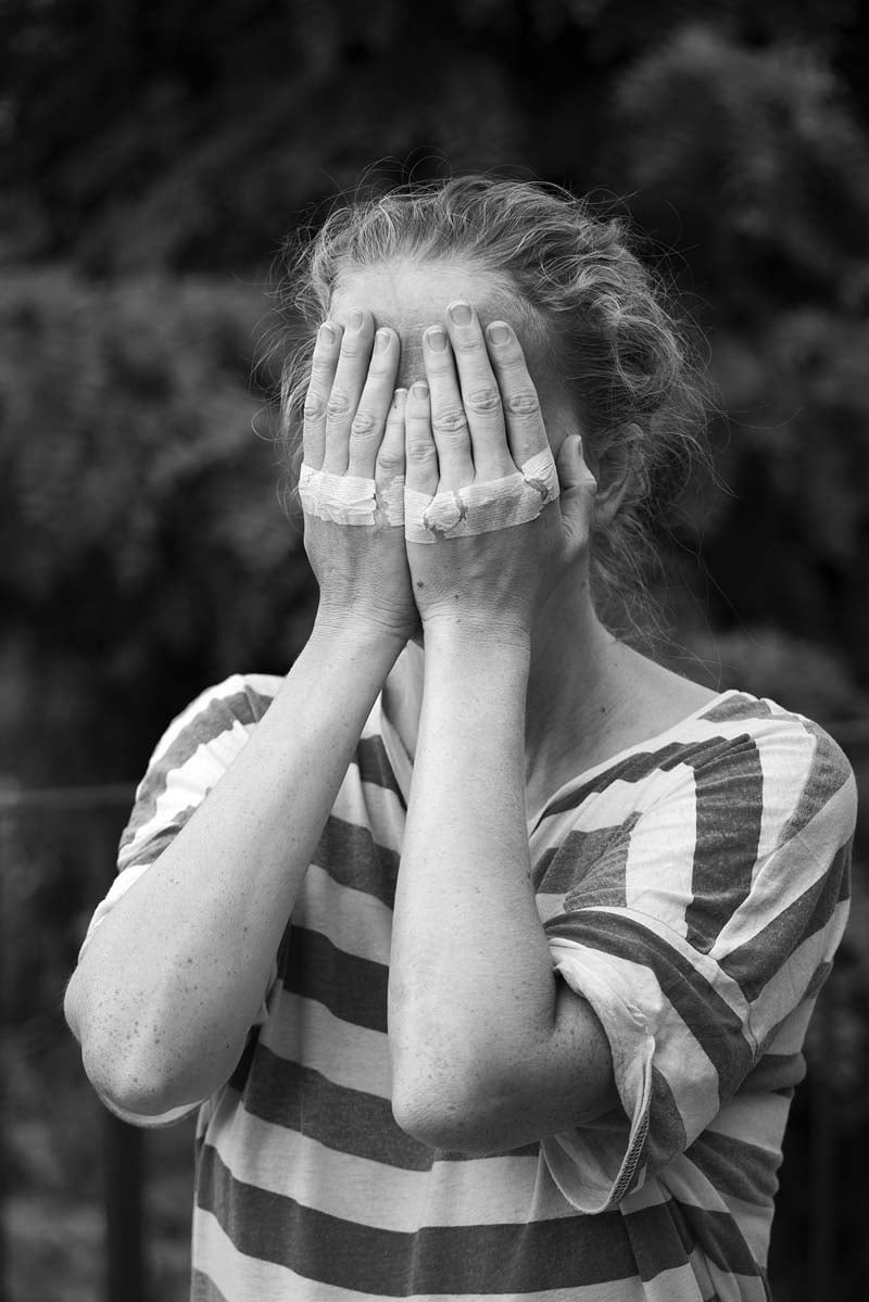 Woman covers her eyes, her hands have strips of masking tape over the knuckles. She wears a striped t-shirt. Photo by Alex Llovet