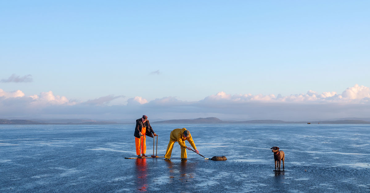 Two fishermen and their dog working on the sand in Morecambe Bay © Tessa Bunney