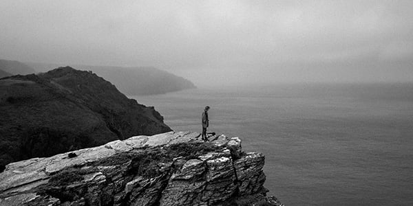Black and white photo by Robert Darch of man standing on jagged cliff rocks looking out into the ocean