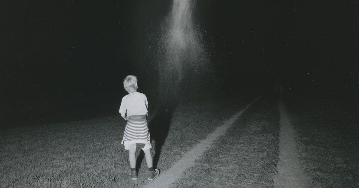 A child stands in a field at night with dirt tracks fading into the distance | Wouter Van de Voorde photography